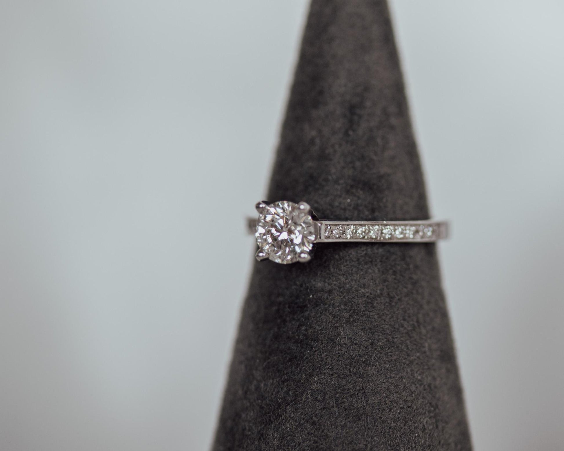 Round brilliant diamond solitaire engagement ring in 14K white gold with pavé band, displayed on dark velvet cone