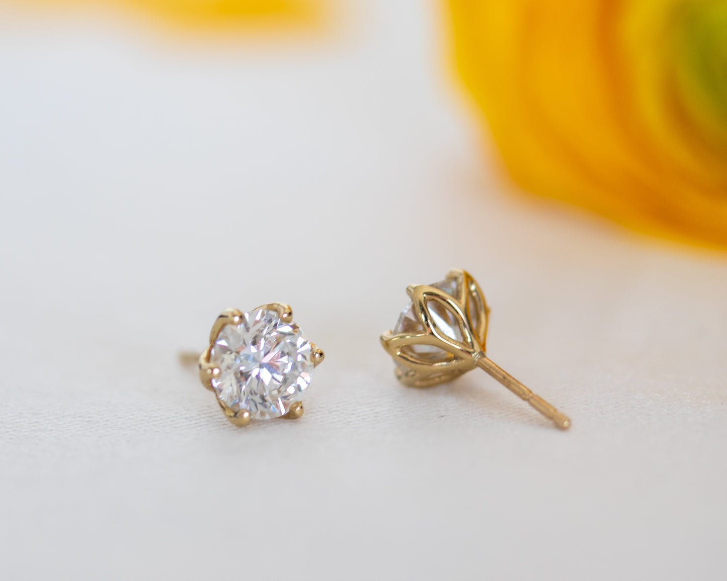 Round brilliant diamond stud earrings in 14K gold, one showing the diamond and one the floral basket