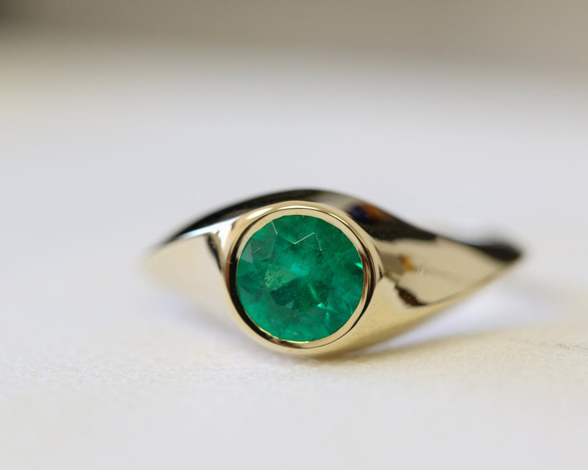 Round natural emerald bezel-set in a twisted yellow gold signet ring, close-up