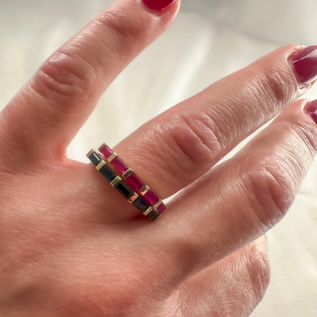 Ruby and blue sapphire baguette bands in 14K gold stacked on the hand