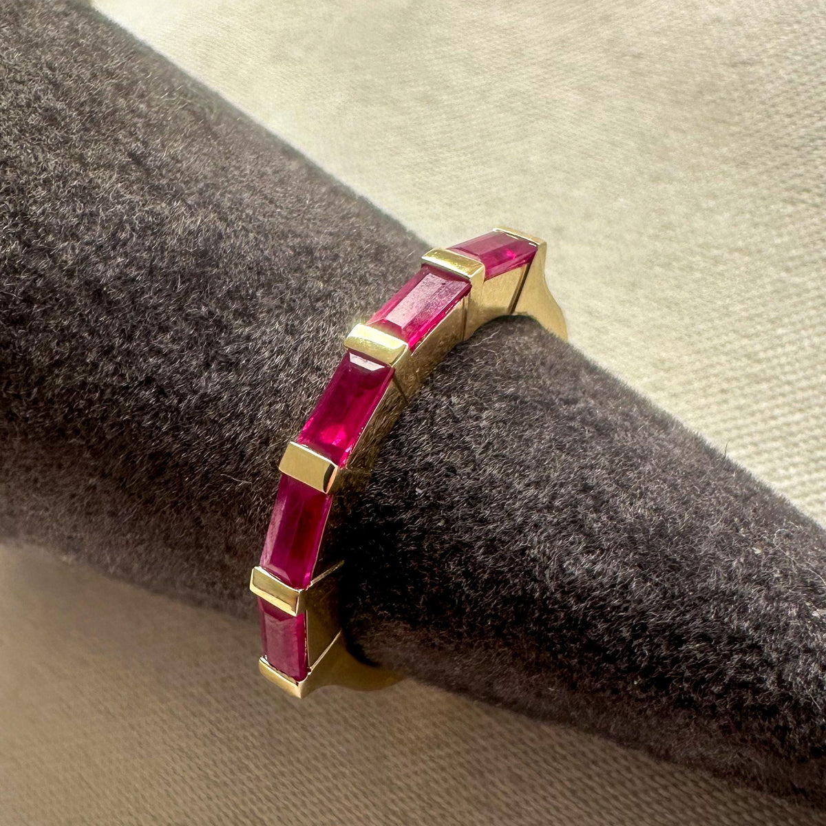 Ruby baguette band in 14K gold on a gray velvet ring display