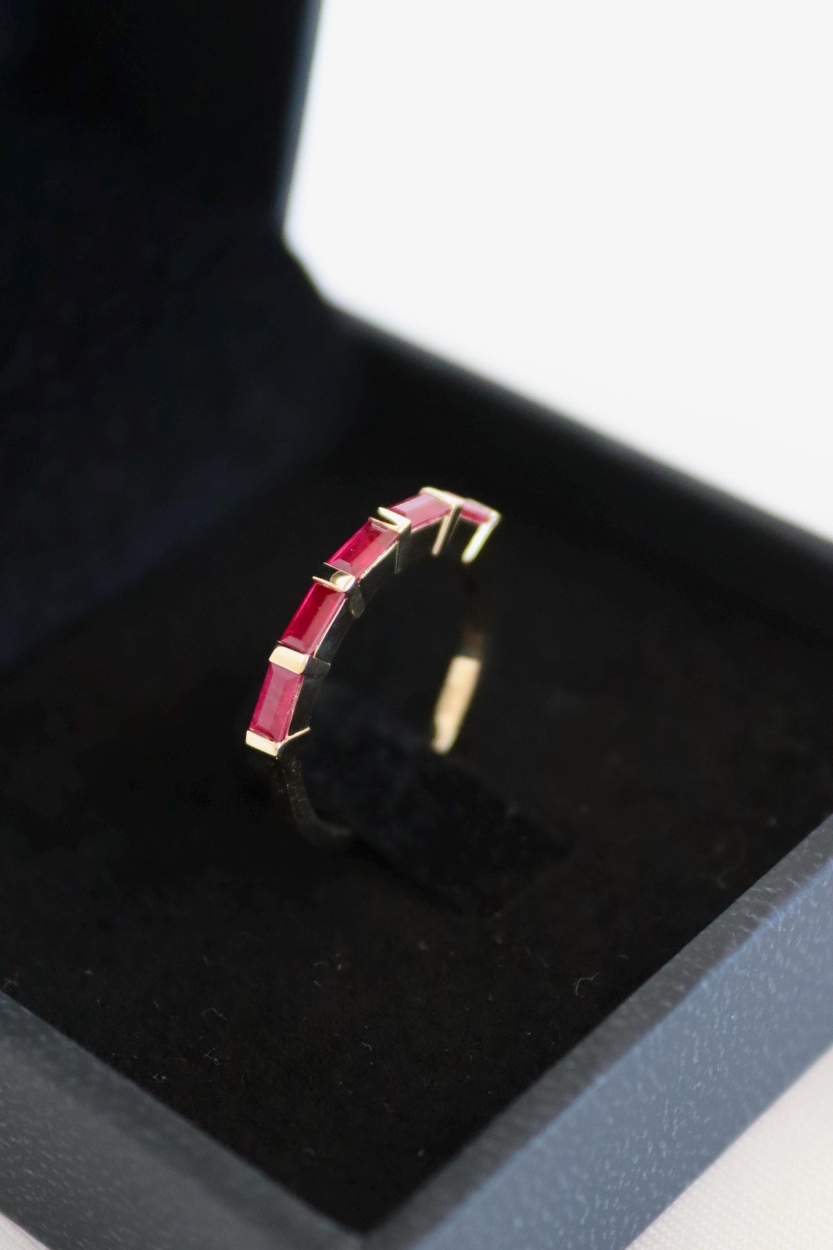 Five ruby baguettes bar-set in a 14K gold band in a black jewelry box