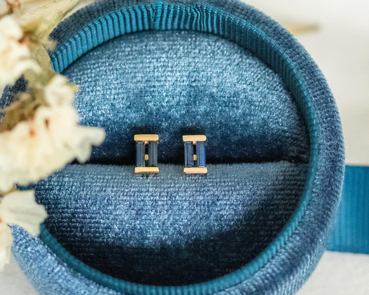 Gold and blue sapphire baguette stud earrings nestled in a blue velvet jewelry box