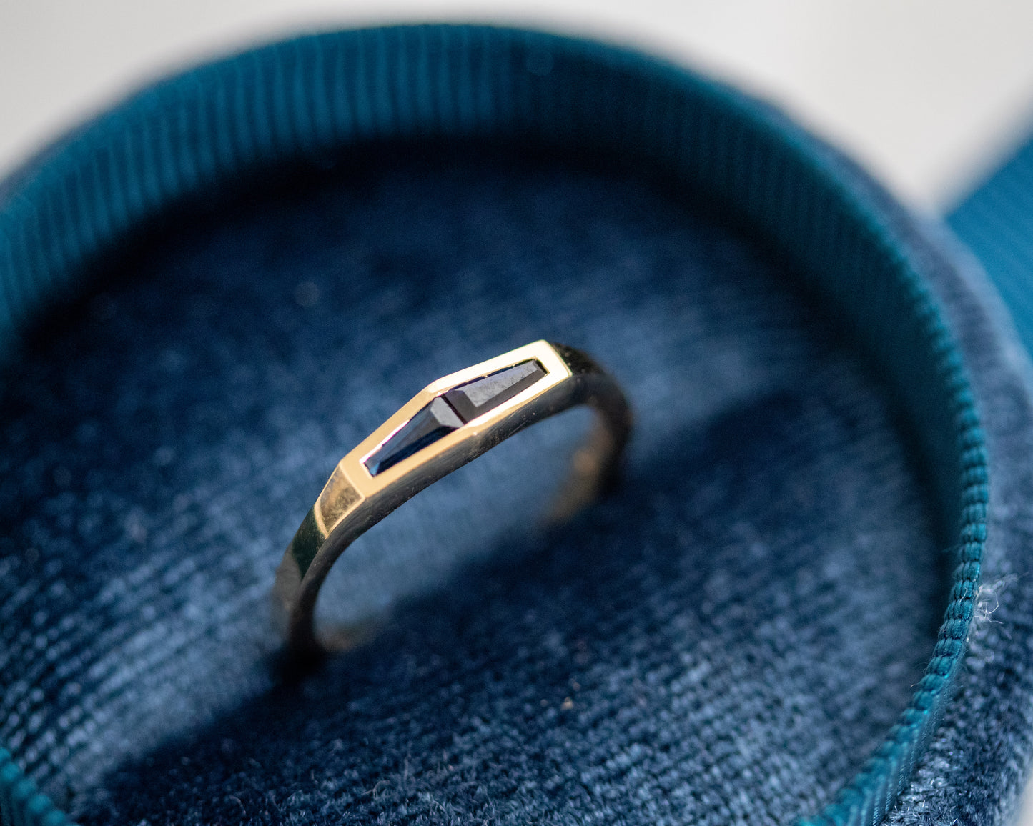 Tapered baguette blue sapphire ring in 14K yellow gold, shown from the front in a blue velvet ring box.
