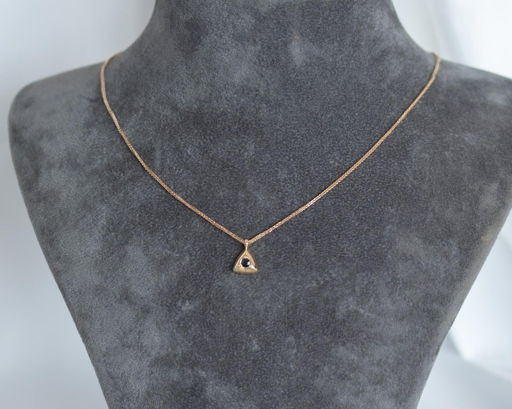 Dainty gold triangle sapphire pendant necklace shown on a neck display