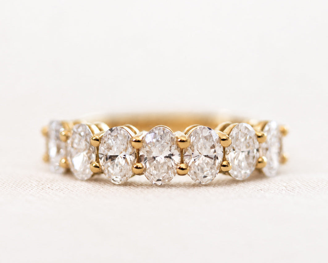 Seven-stone oval-cut diamond ring in gold, angled view on a light surface