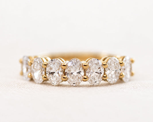 Seven-stone oval-cut diamond ring in gold, angled view on a light surface