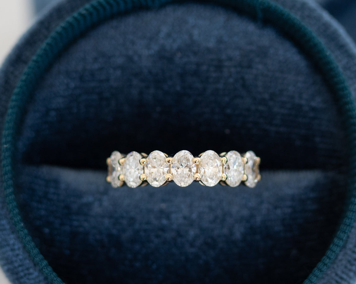 Gold seven-stone oval-cut diamond ring displayed in a teal jewelry box