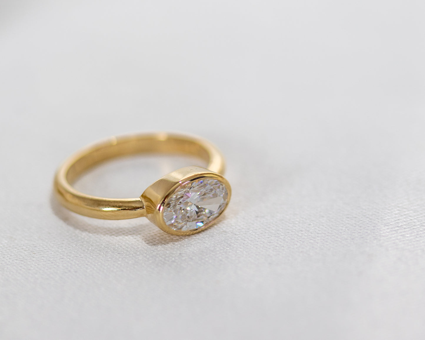 Side view of oval diamond bezel-set engagement ring in 14K yellow gold — minimalist fine jewelry by Rotem Avitan.