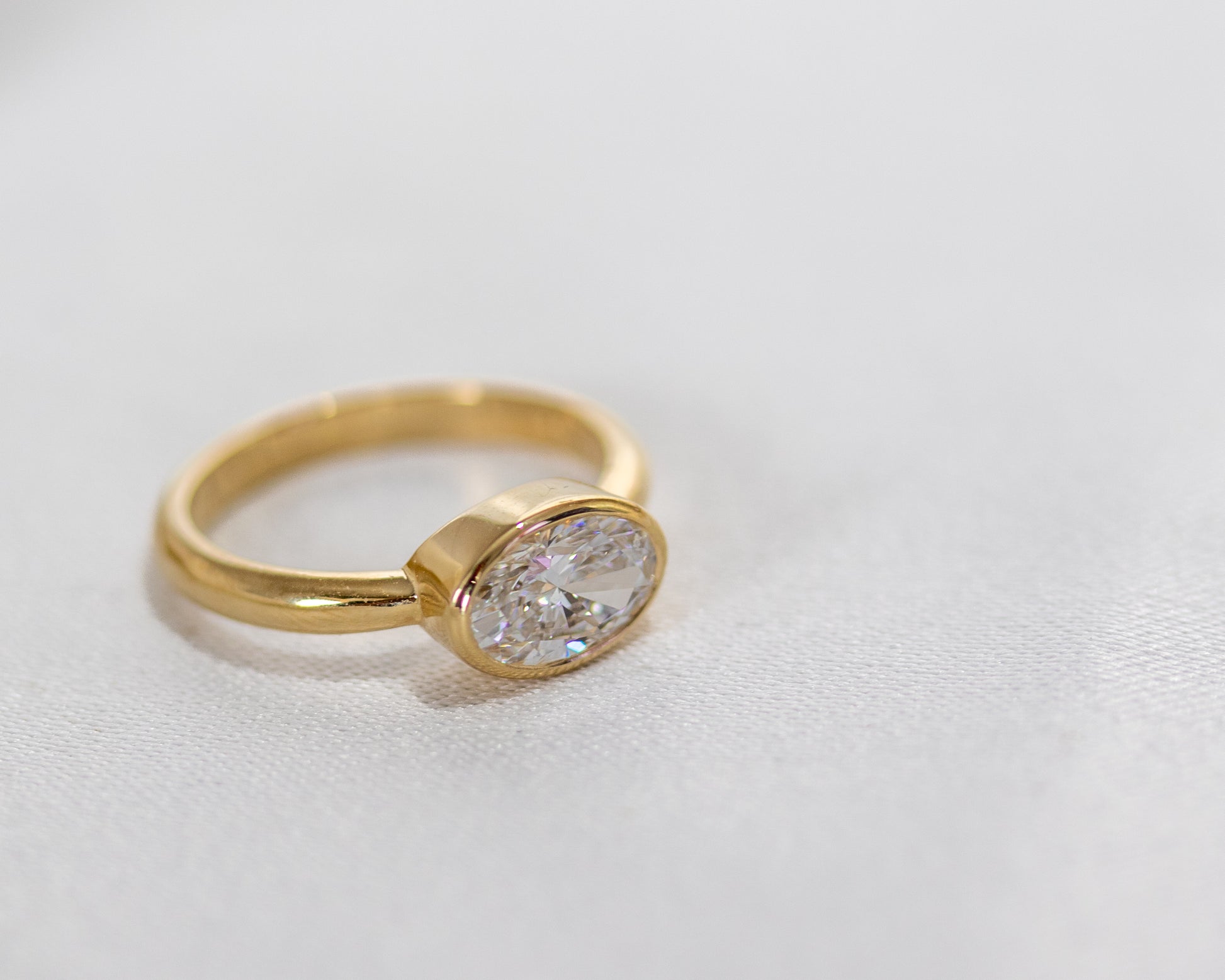 Side view of oval diamond bezel-set engagement ring in 14K yellow gold — minimalist fine jewelry by Rotem Avitan.