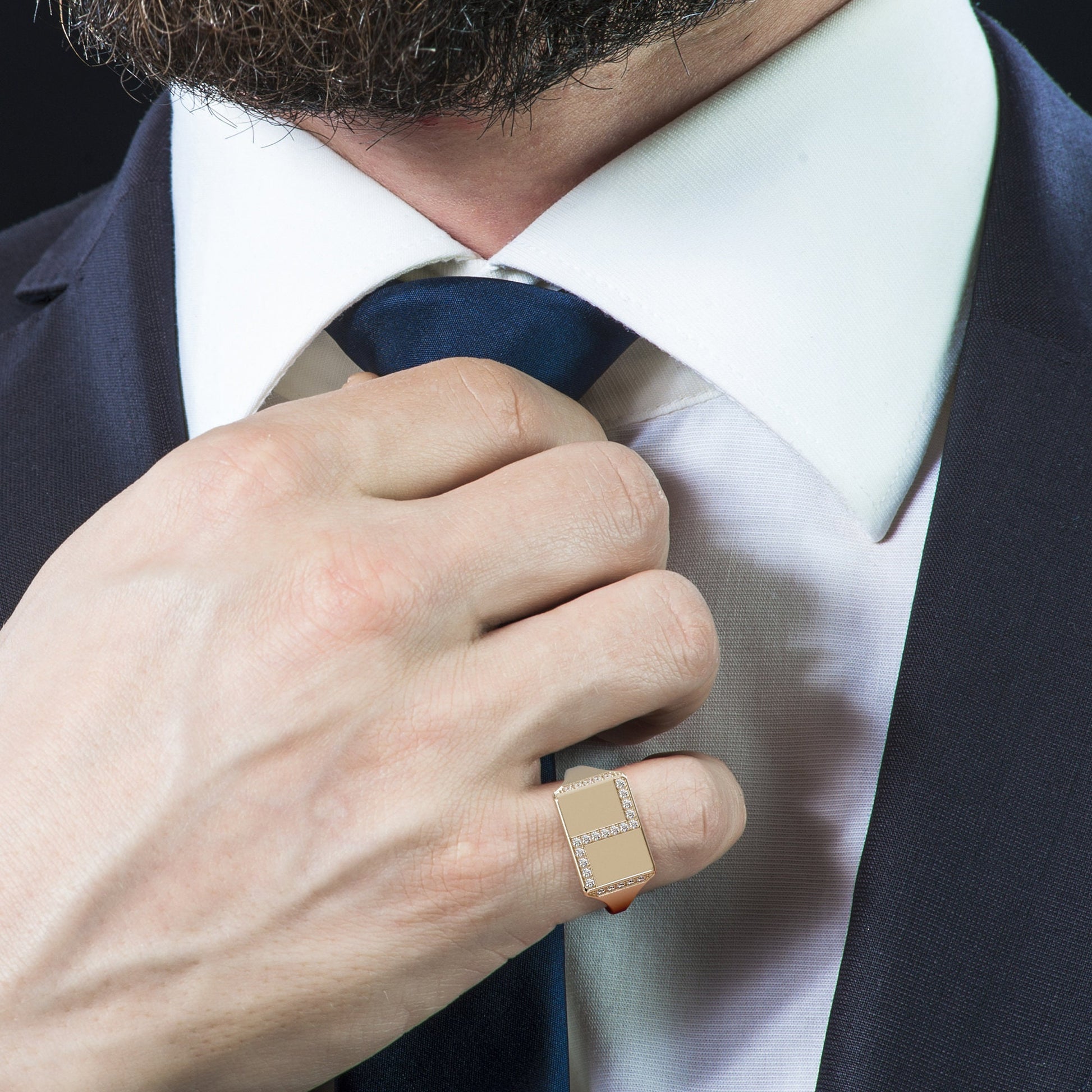 Man wearing a white diamond pave signet ring in 14K gold while adjusting his tie