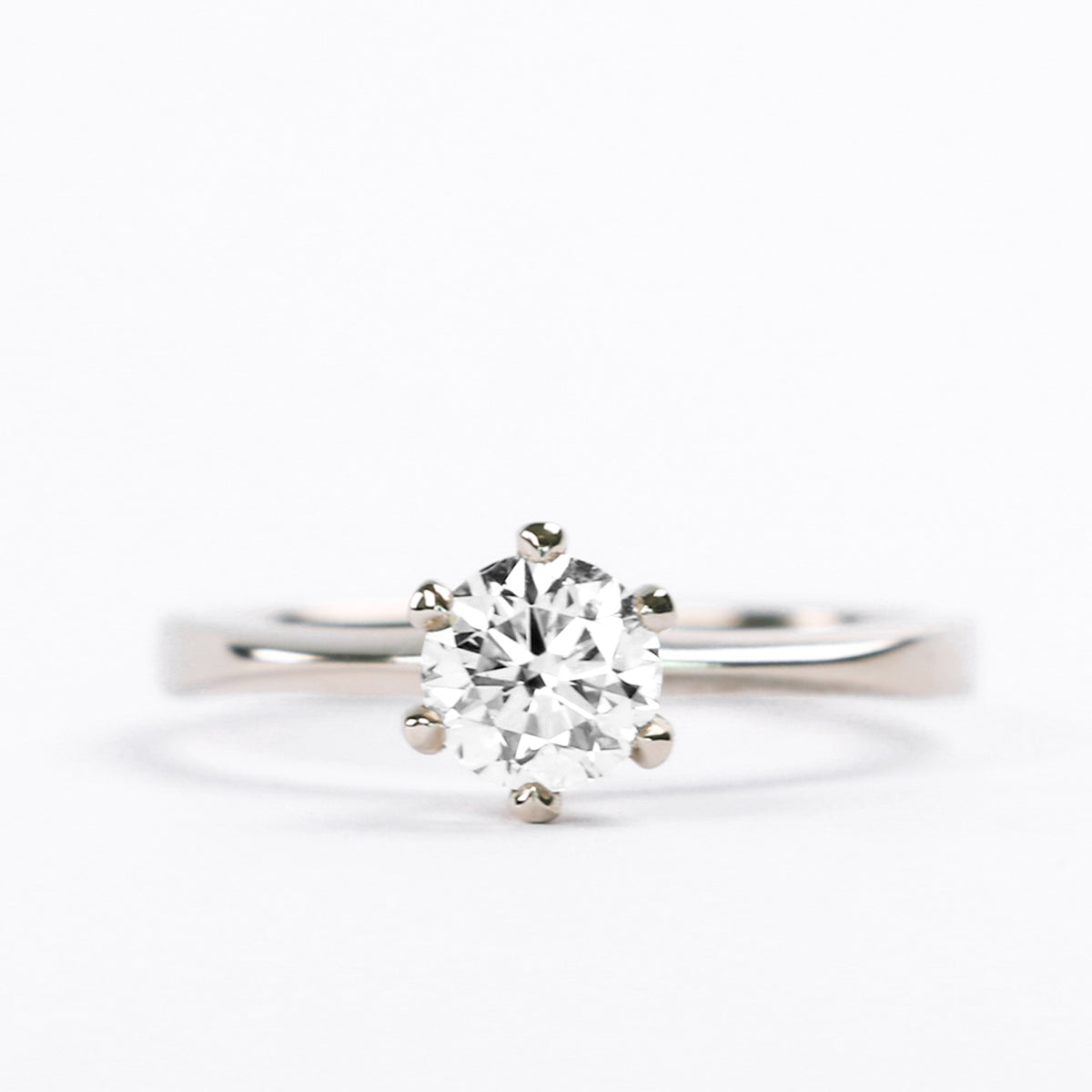 Six-prong round diamond solitaire engagement ring on a flat white gold band, front view
