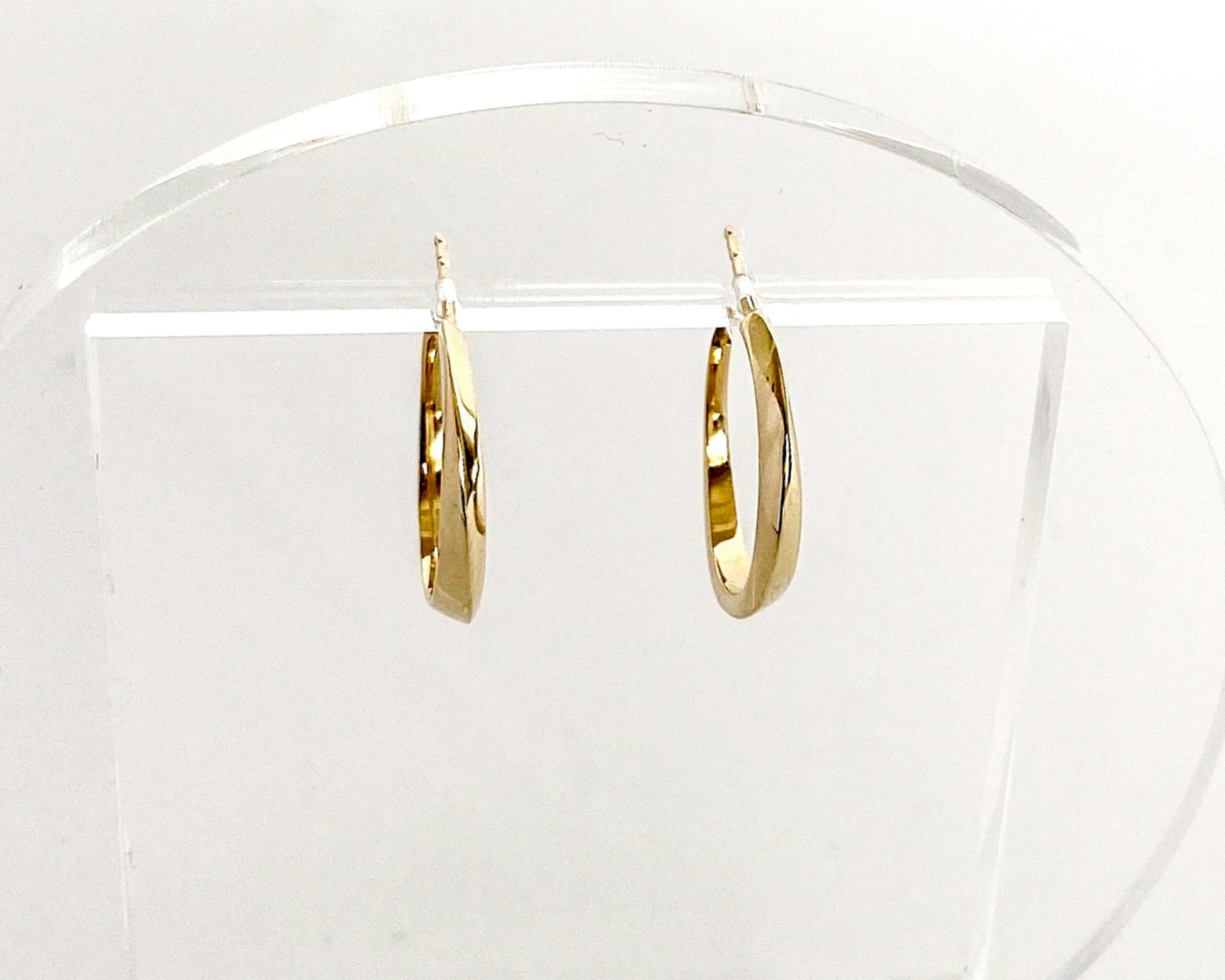 Small 14K gold twist hoop earrings with polished geometric curves, minimalist modern fine jewelry displayed on a clear acrylic stand.