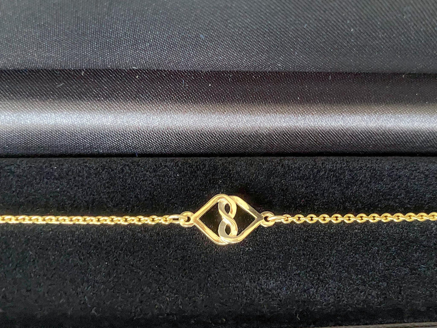 Gold bracelet with a unique charm design on a black satin background