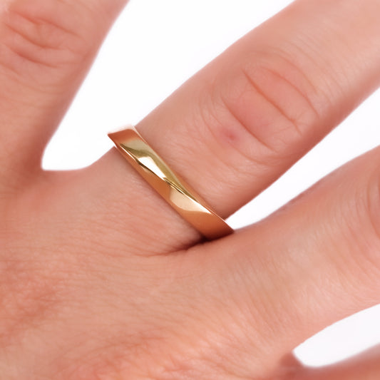 A close-up image of a person's finger wearing a 18K yellow gold geometric wedding band with a twisted trianglish structure.