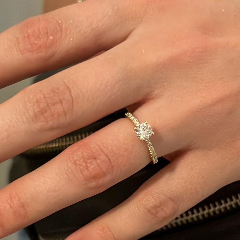 Close-up image of a hand wearing a 14K gold diamond engagement ring with a natural diamond center stone and diamond band.