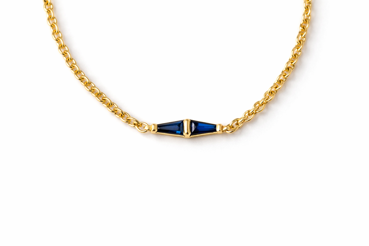 Two tapered baguette blue sapphires meeting at the center of a yellow gold rolo chain bracelet