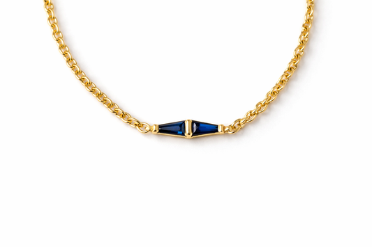 Two tapered baguette blue sapphires meeting at the center of a yellow gold rolo chain bracelet