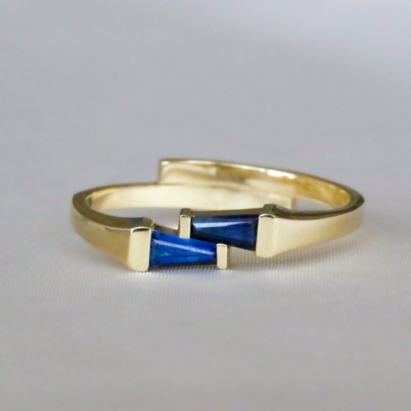 A gold ring with two blue sapphires set cheek to cheek.