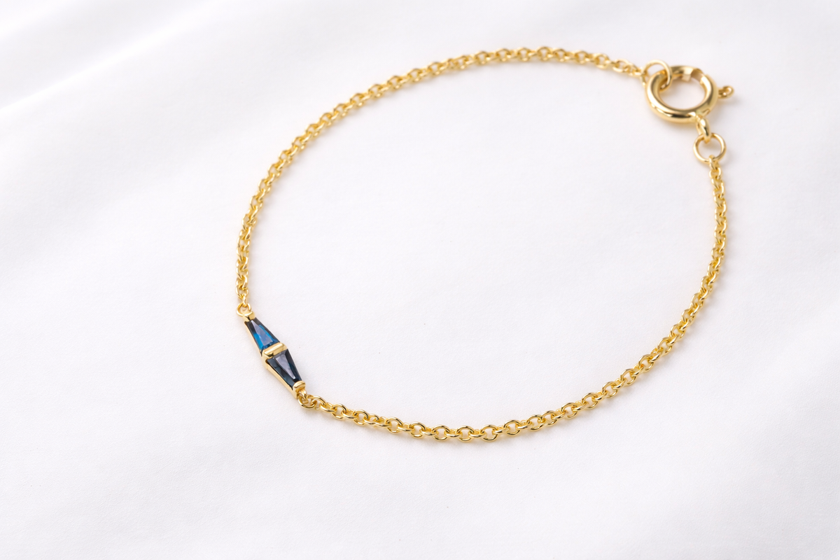 Yellow gold rolo chain bracelet with two blue sapphires meeting at the center, full length on white