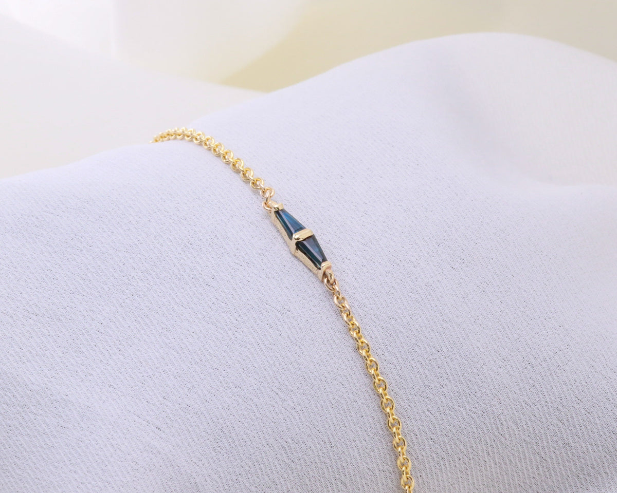 Yellow gold bracelet with two tapered baguette blue sapphires resting on white fabric