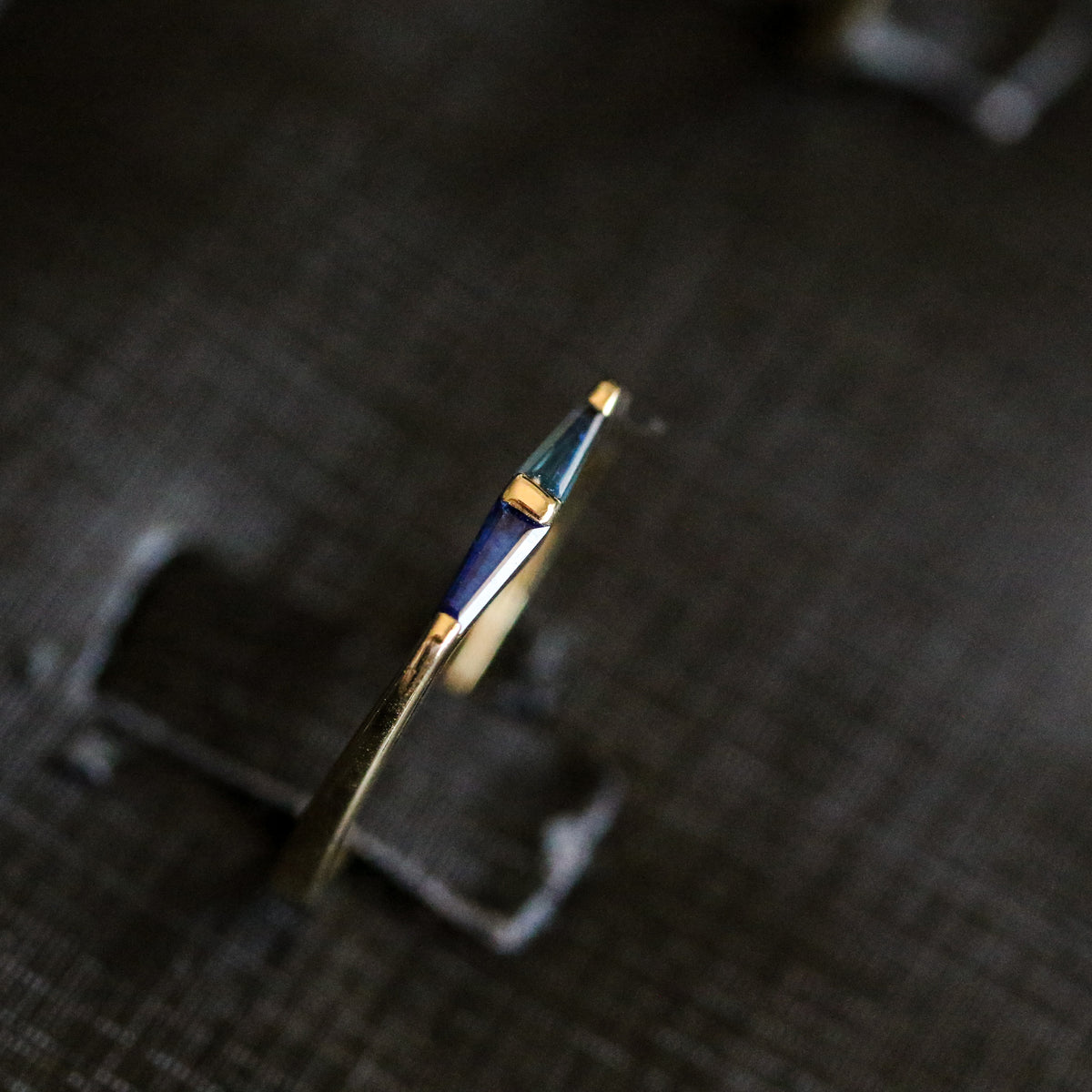 Side view of a 14K gold ring with two tapered baguette blue sapphires, on a dark background