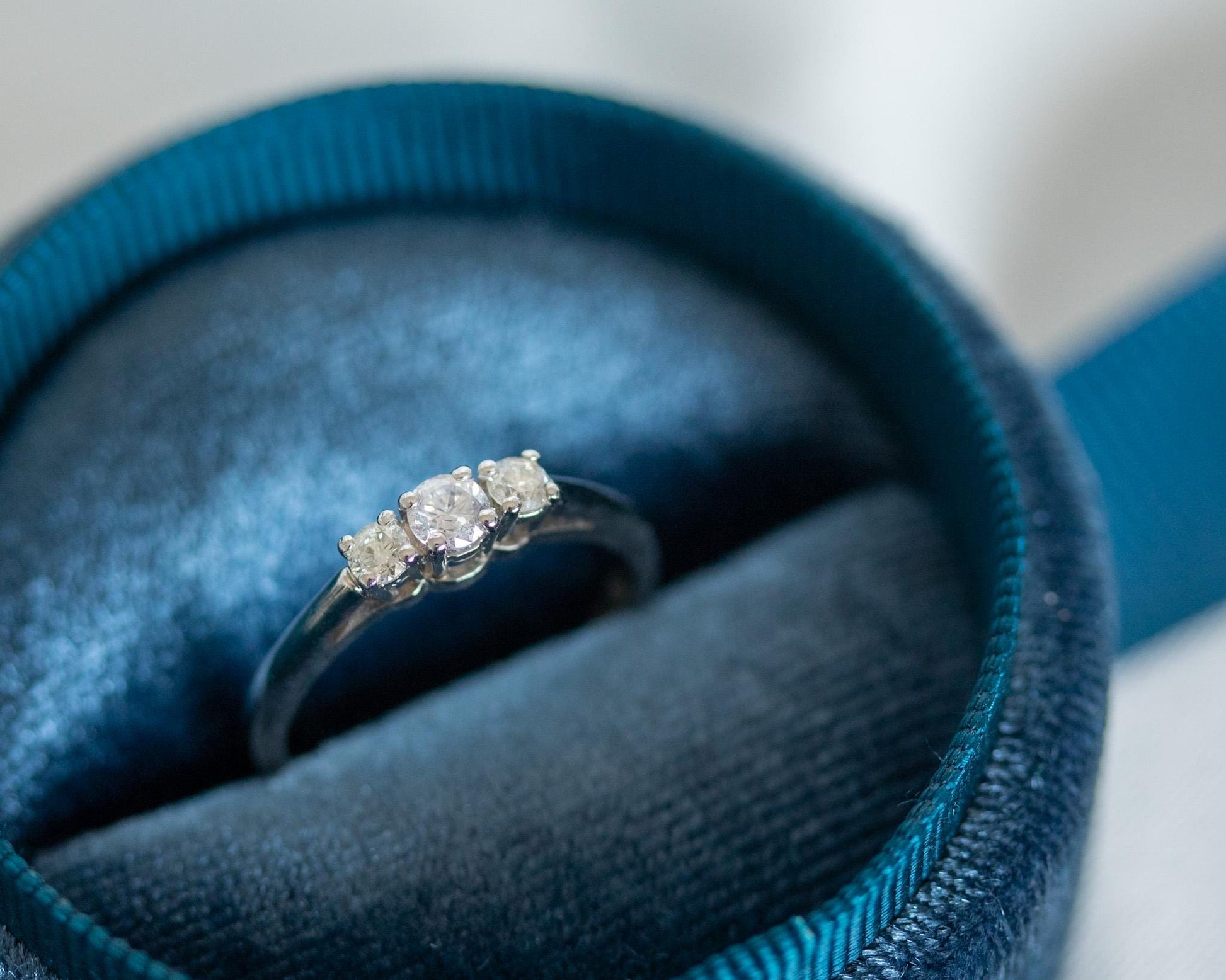 Three-stone diamond engagement ring in 14K white gold displayed in blue velvet jewelry box, classic trilogy design with round brilliant diamonds