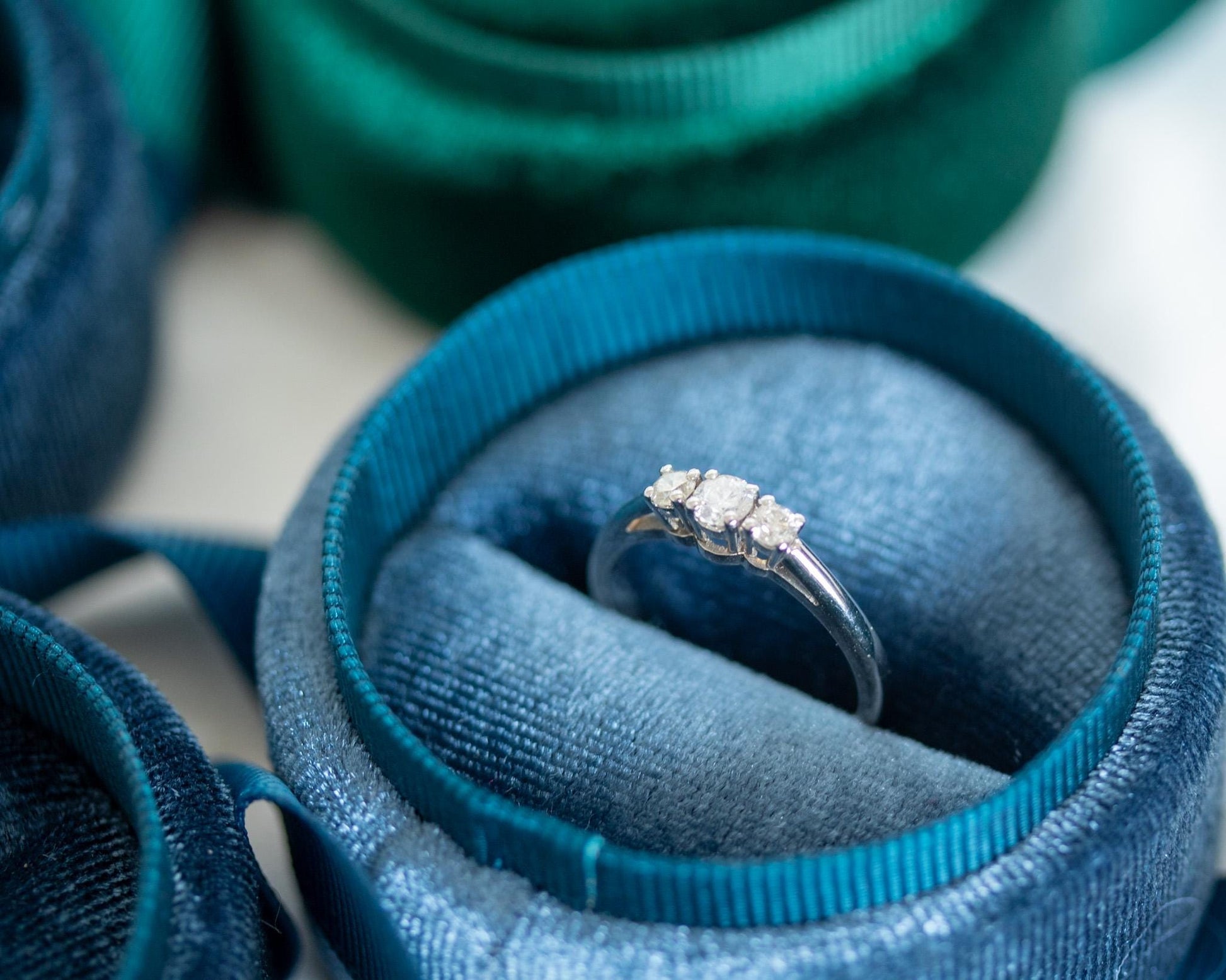 Three-stone diamond engagement ring in 14K white gold, elegant trilogy design displayed in blue and green velvet jewelry boxes