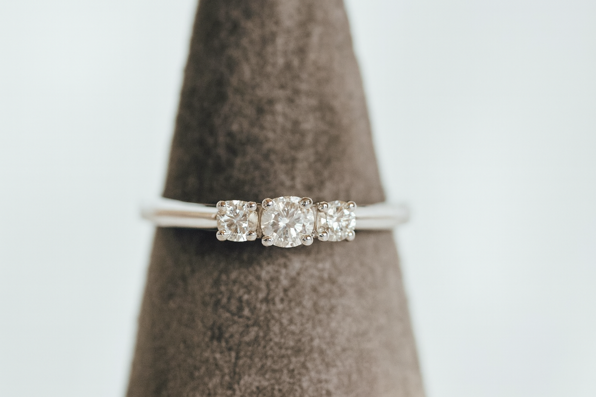 White gold three-stone diamond ring on a grey ring display cone