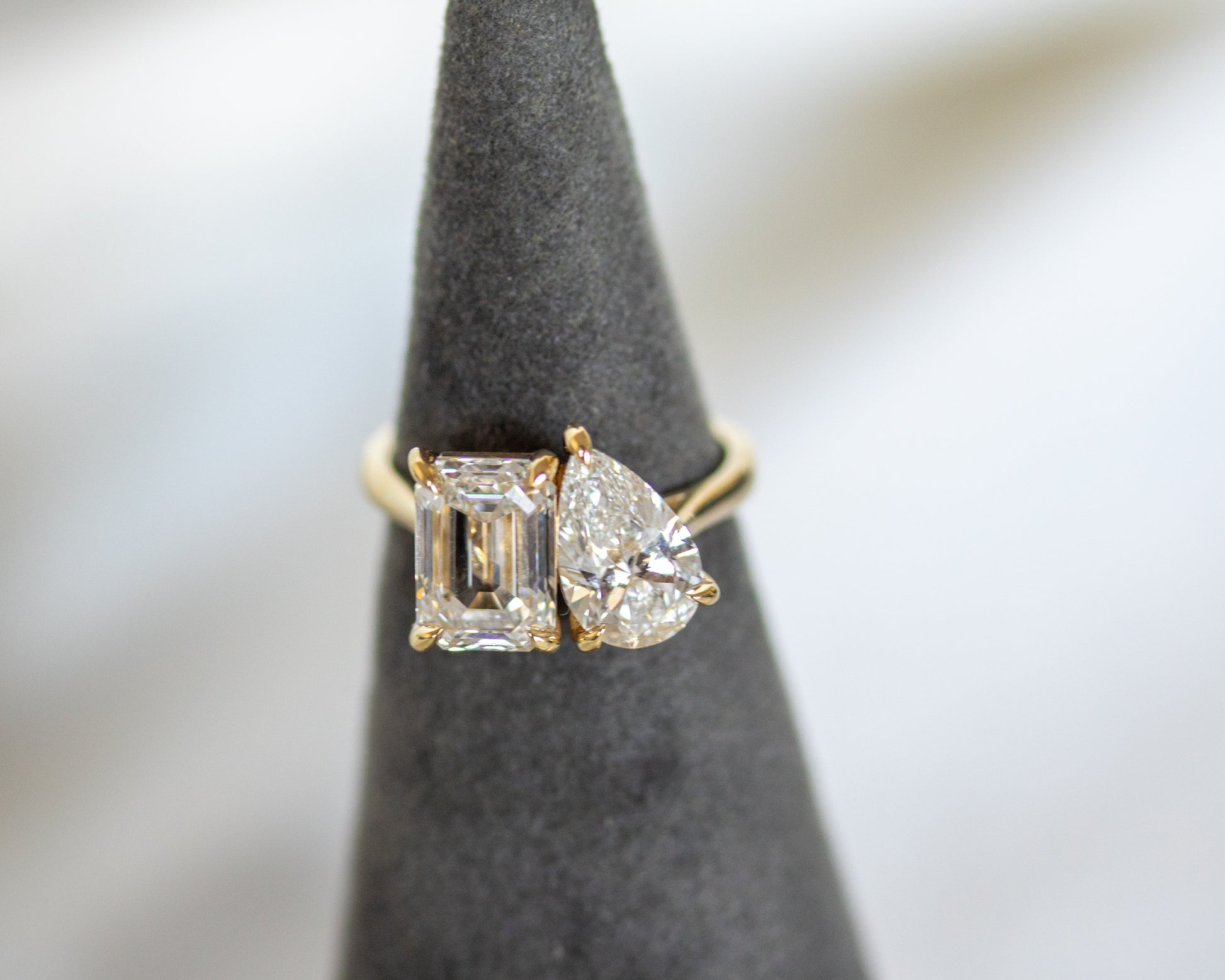 Toi et Moi emerald and pear diamond ring in 14K yellow gold on a display stand