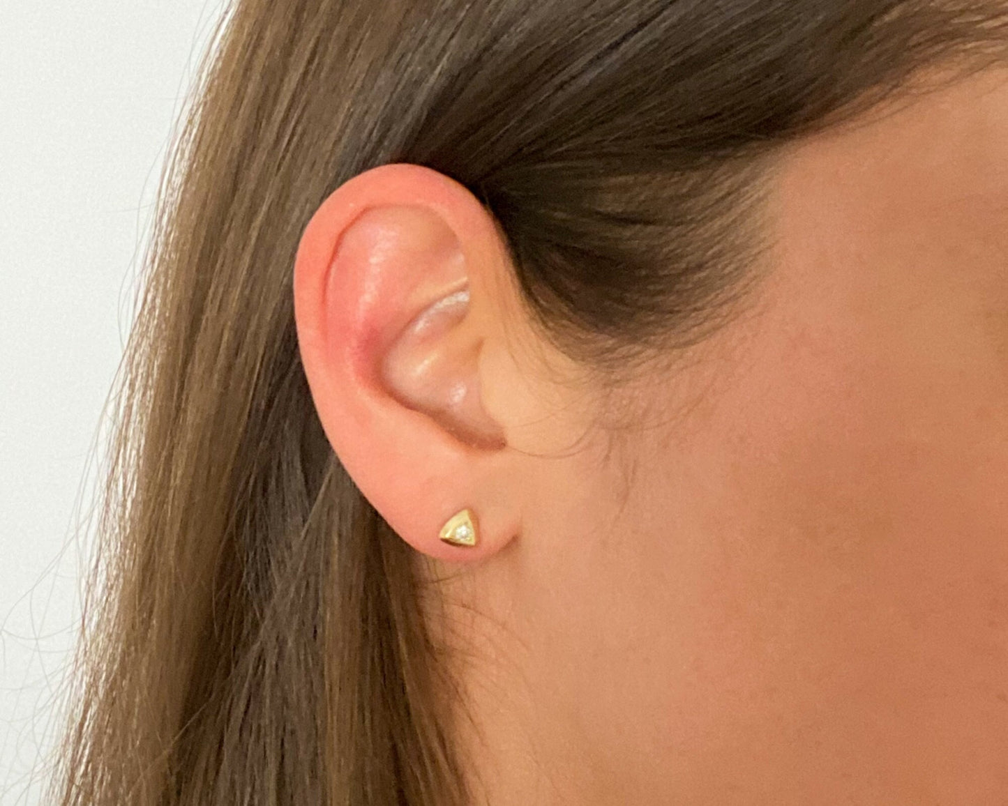 Triangular gold diamond stud earring worn on the ear