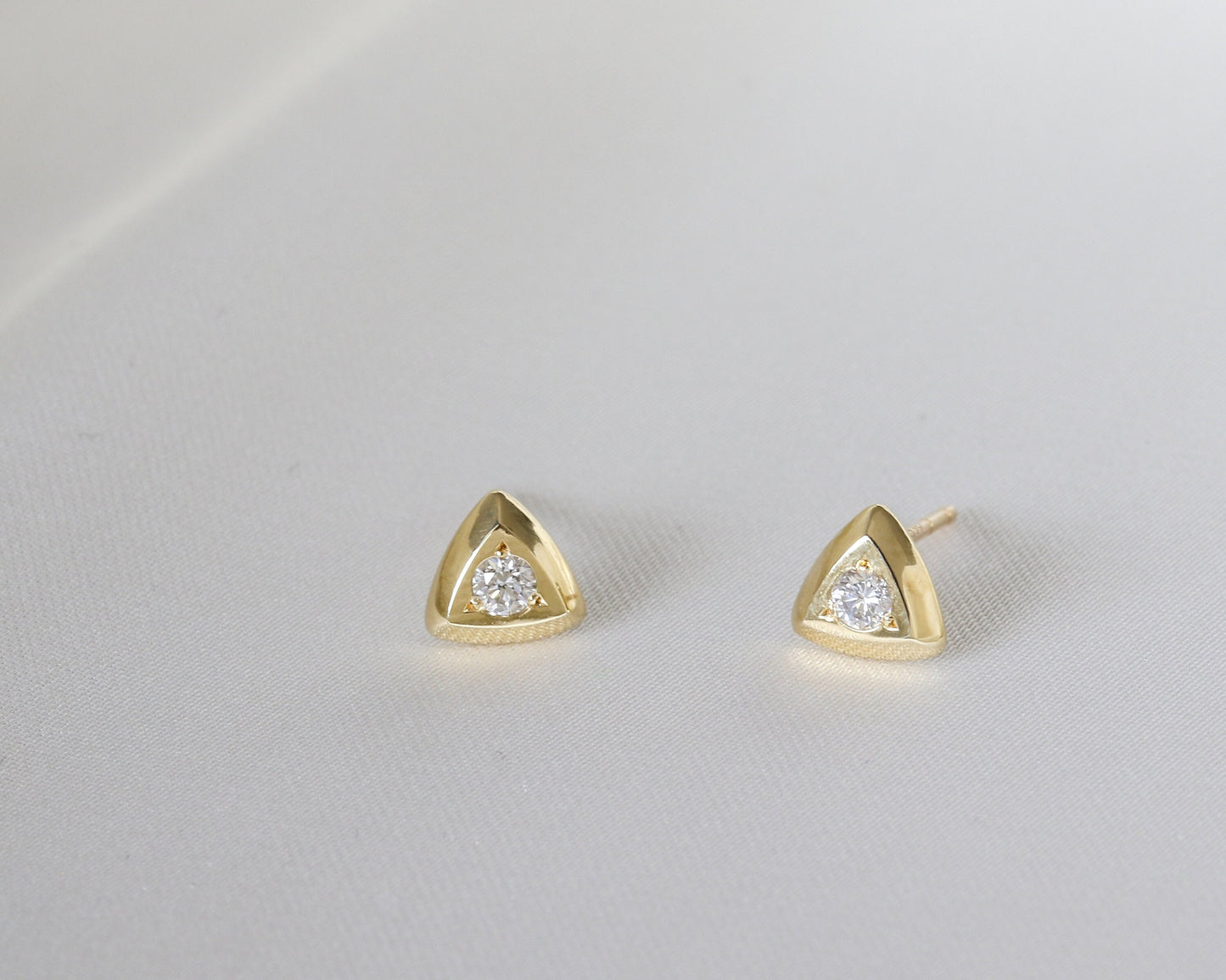 Close-up of two 14K gold triangular studs with round diamonds