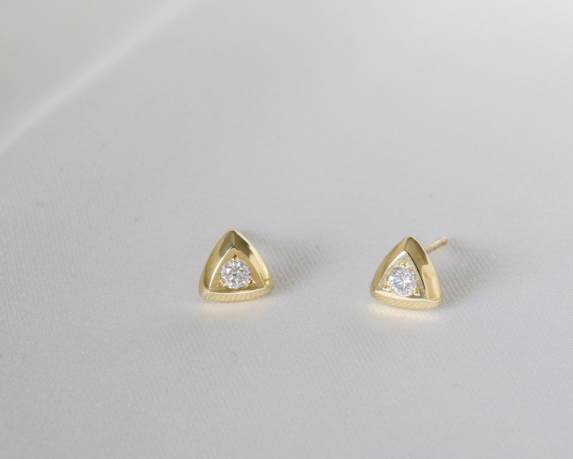 Close-up of two 14K gold triangular studs with round diamonds