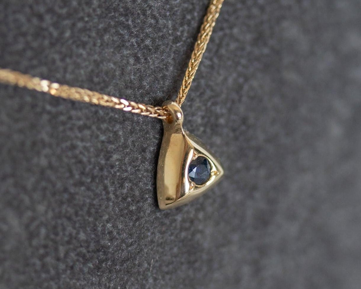 Close-up of a gold triangle pendant set with a round blue sapphire on a fine chain