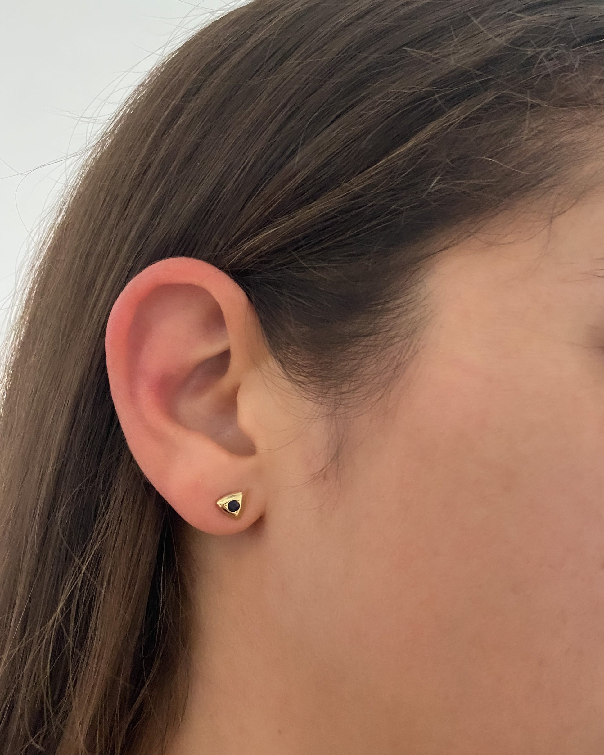 Triangular gold sapphire stud earring worn on the ear