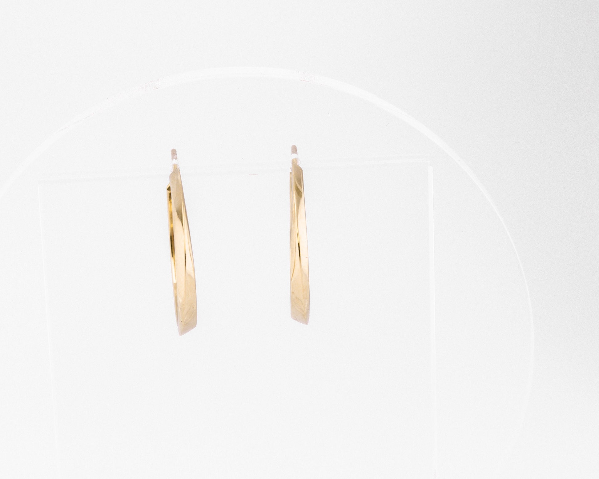 Minimalist 14K gold hoop earrings from the Twist collection, geometric sculpted design displayed on a clear acrylic stand with soft white lighting.