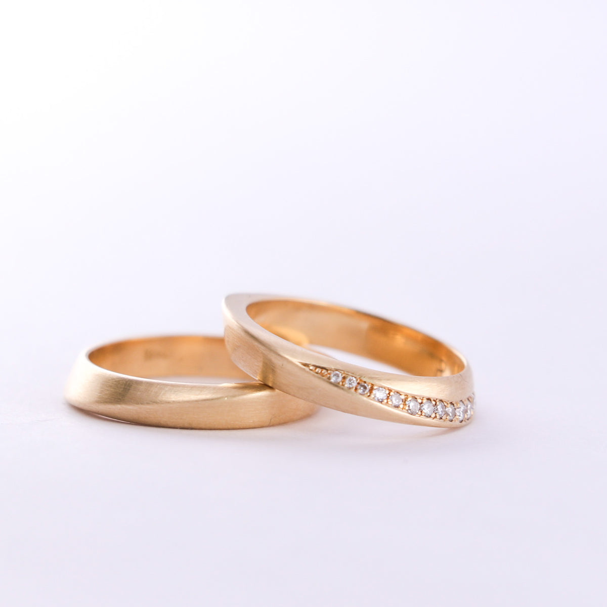 Two twisted gold wedding bands, one with pavé diamonds, on a white background