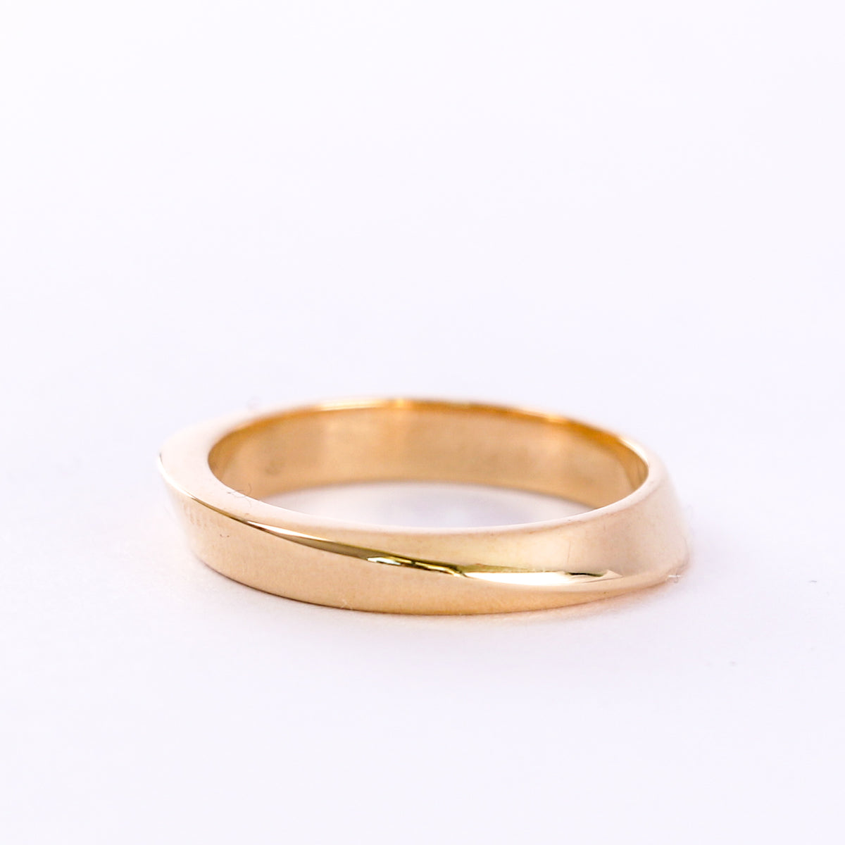 Twisted yellow gold wedding band on a white background, angled view