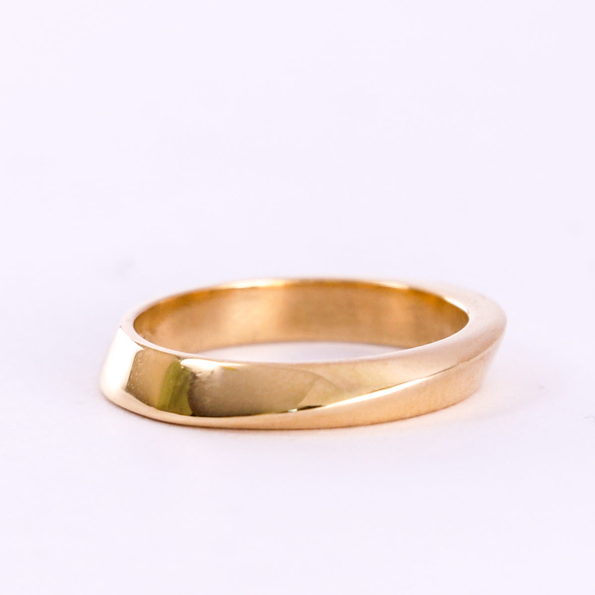 Twisted yellow gold wedding band on a white background, side view