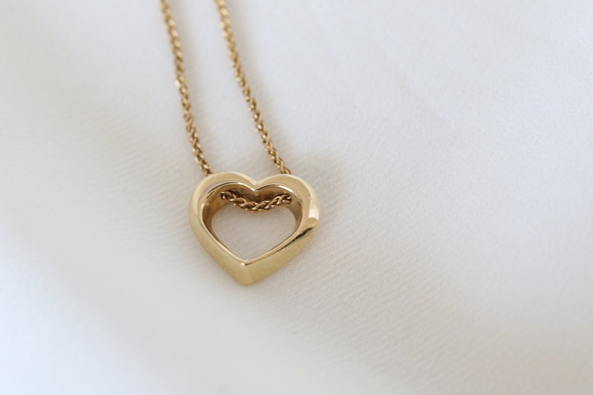 Twisted open heart pendant in 14K yellow gold on a spiga chain, close-up on white