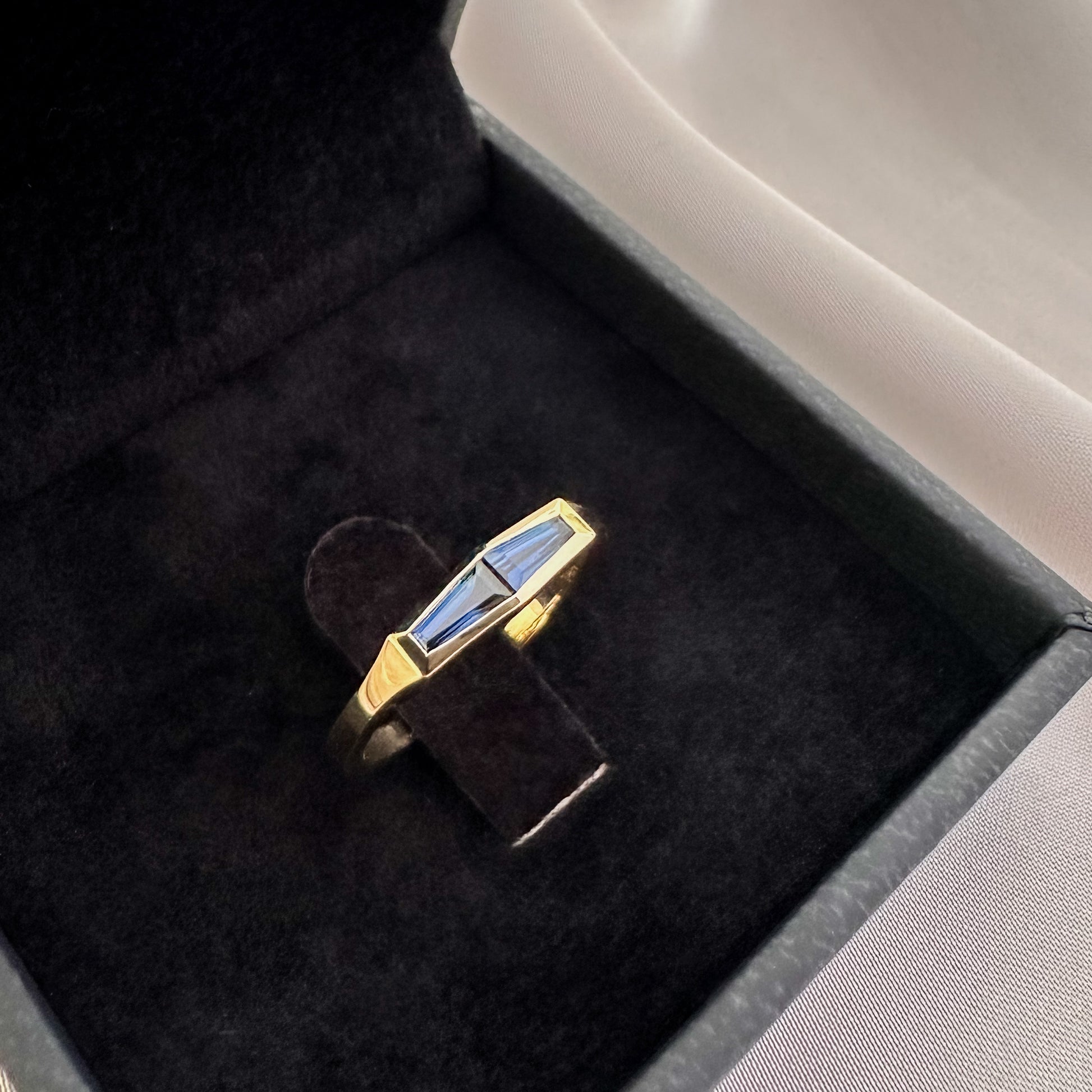 A minimalist gold ring with two blue baguette cut sapphires set in a box, with the ring displaying a tapered design.