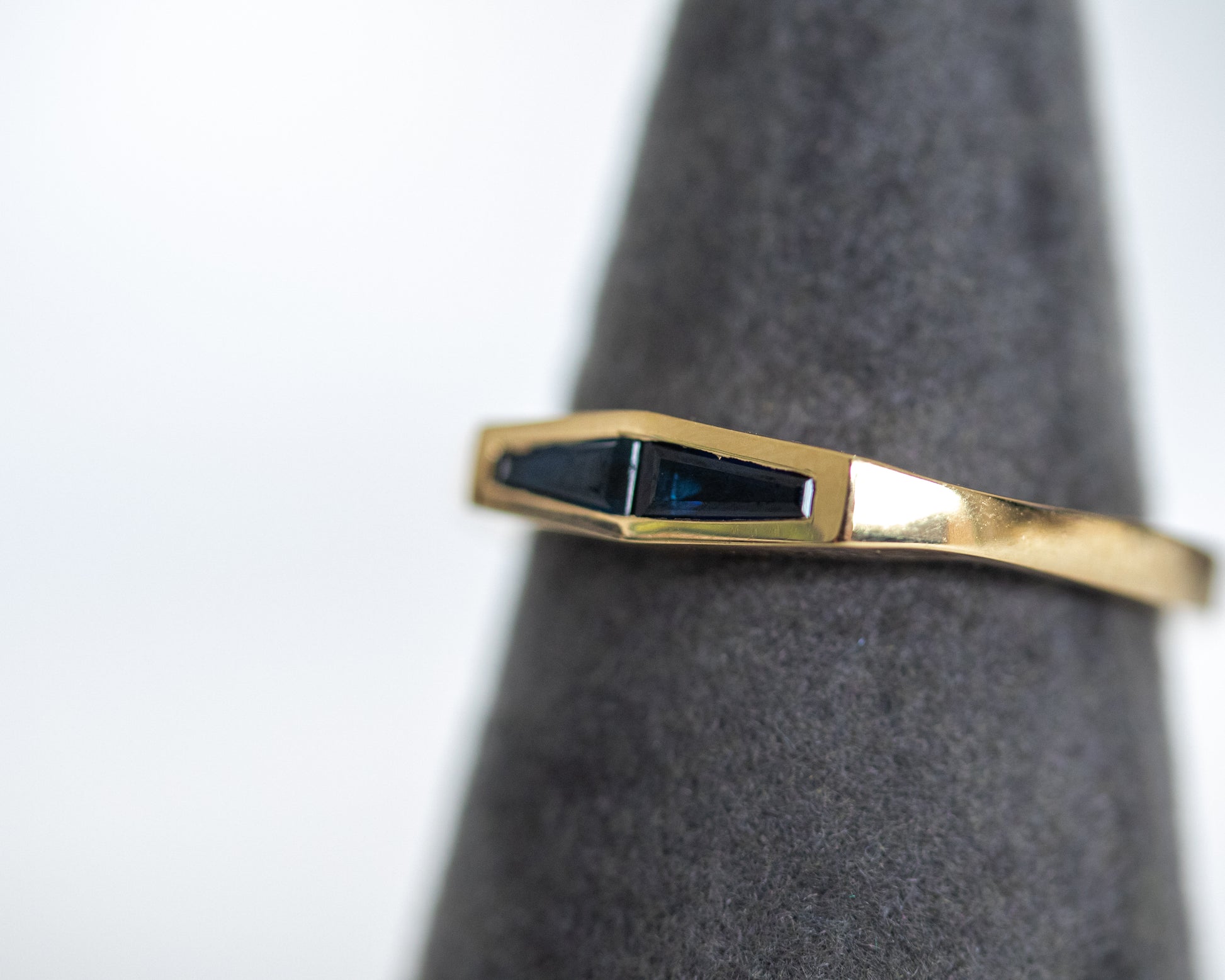 Two natural blue sapphires in a 14K yellow gold band, shown on a grey display stand.