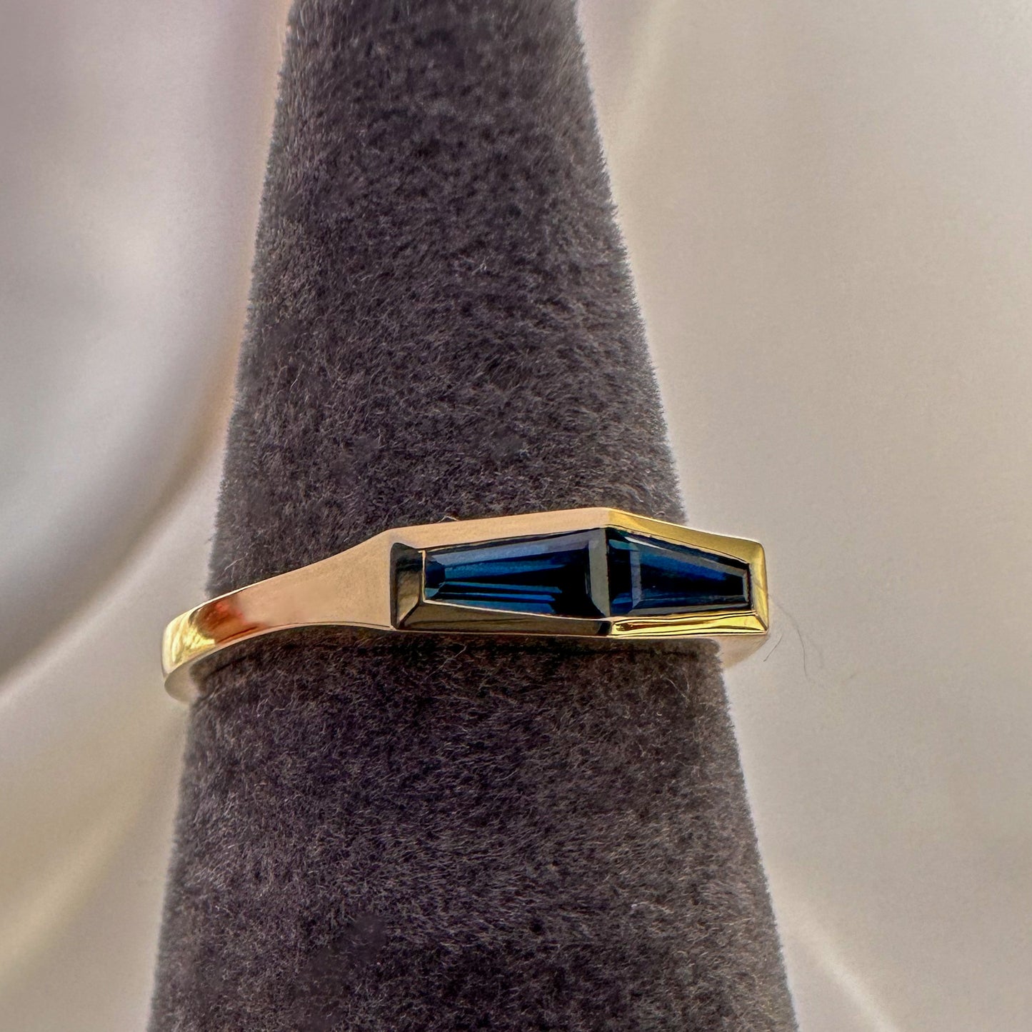 A minimalist gold ring with two blue baguette cut sapphires on gray textures ring stand