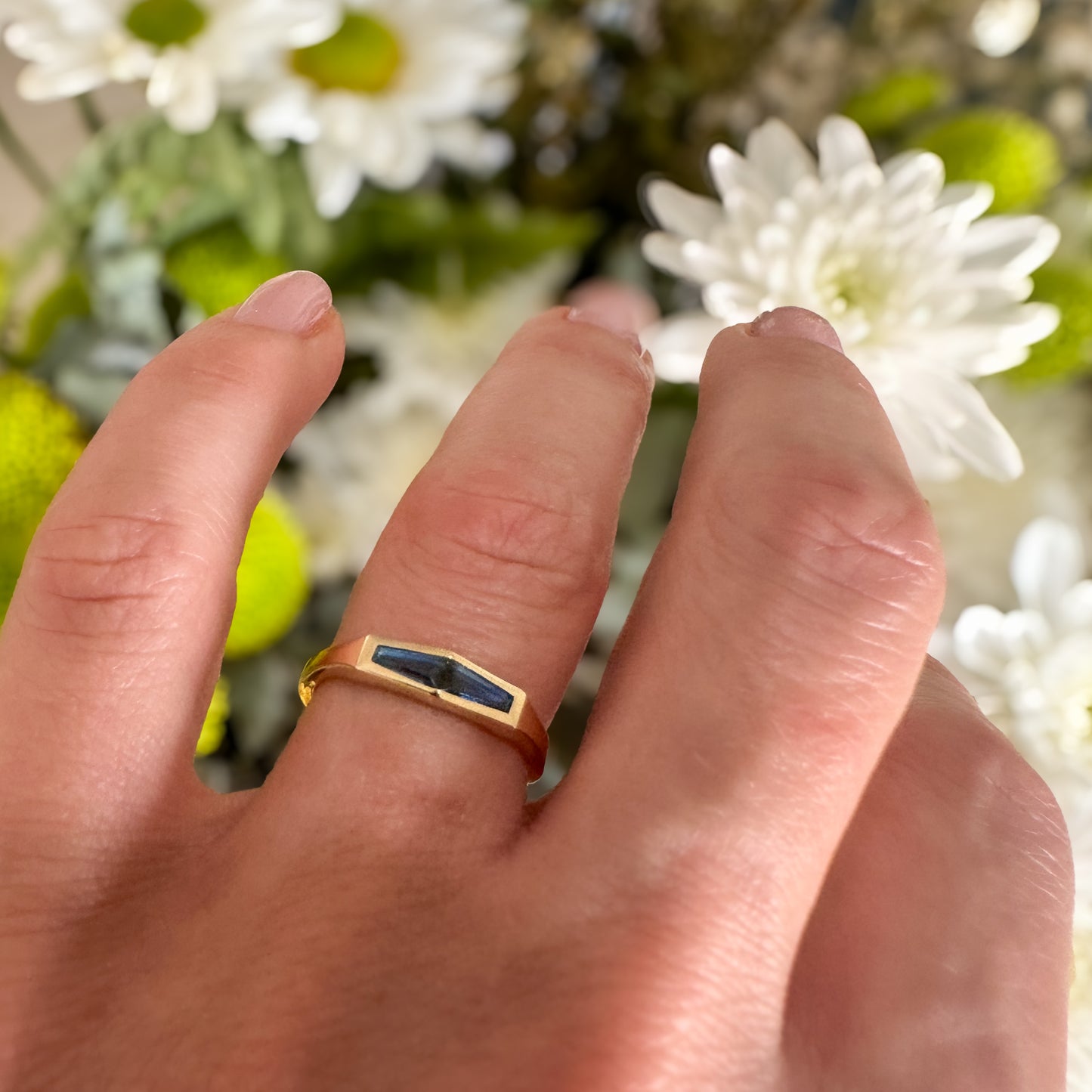 A minimalist gold ring with two blue baguette cut sapphires on womens hand with white flowers in the background