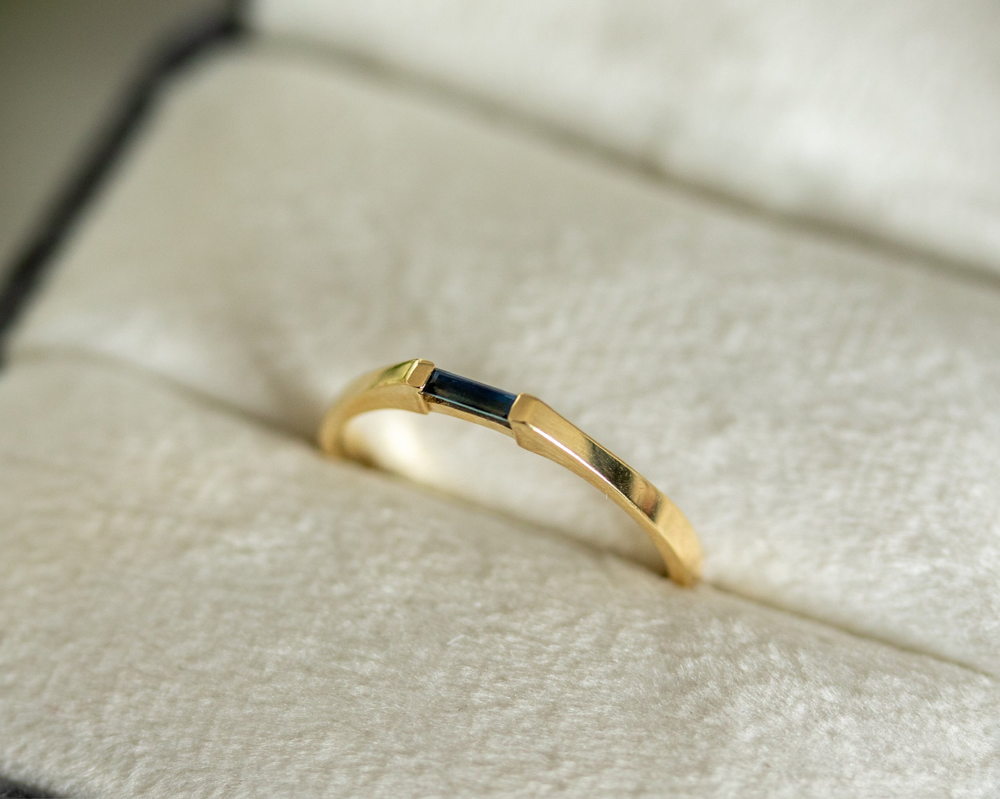 Gold ring with a dark stone on a textured beige surface