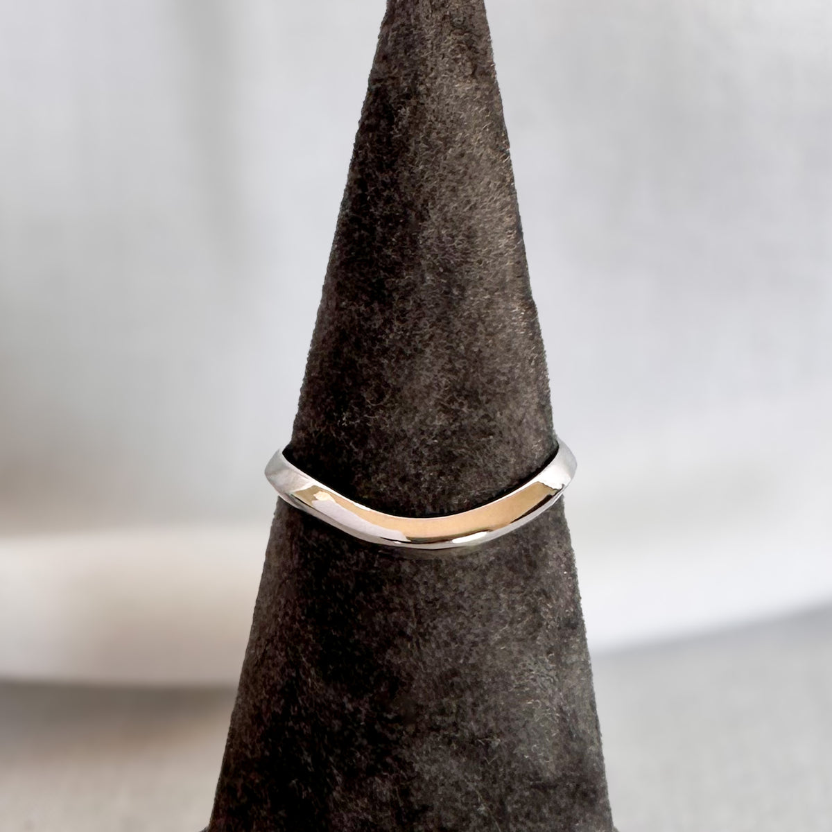 White gold curved wedding band with a wave at the center, on a grey velvet ring cone