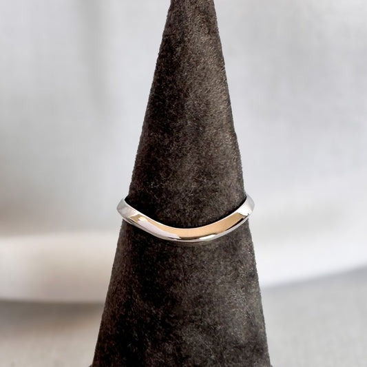 White gold curved wedding band with a wave at the center, on a grey velvet ring cone