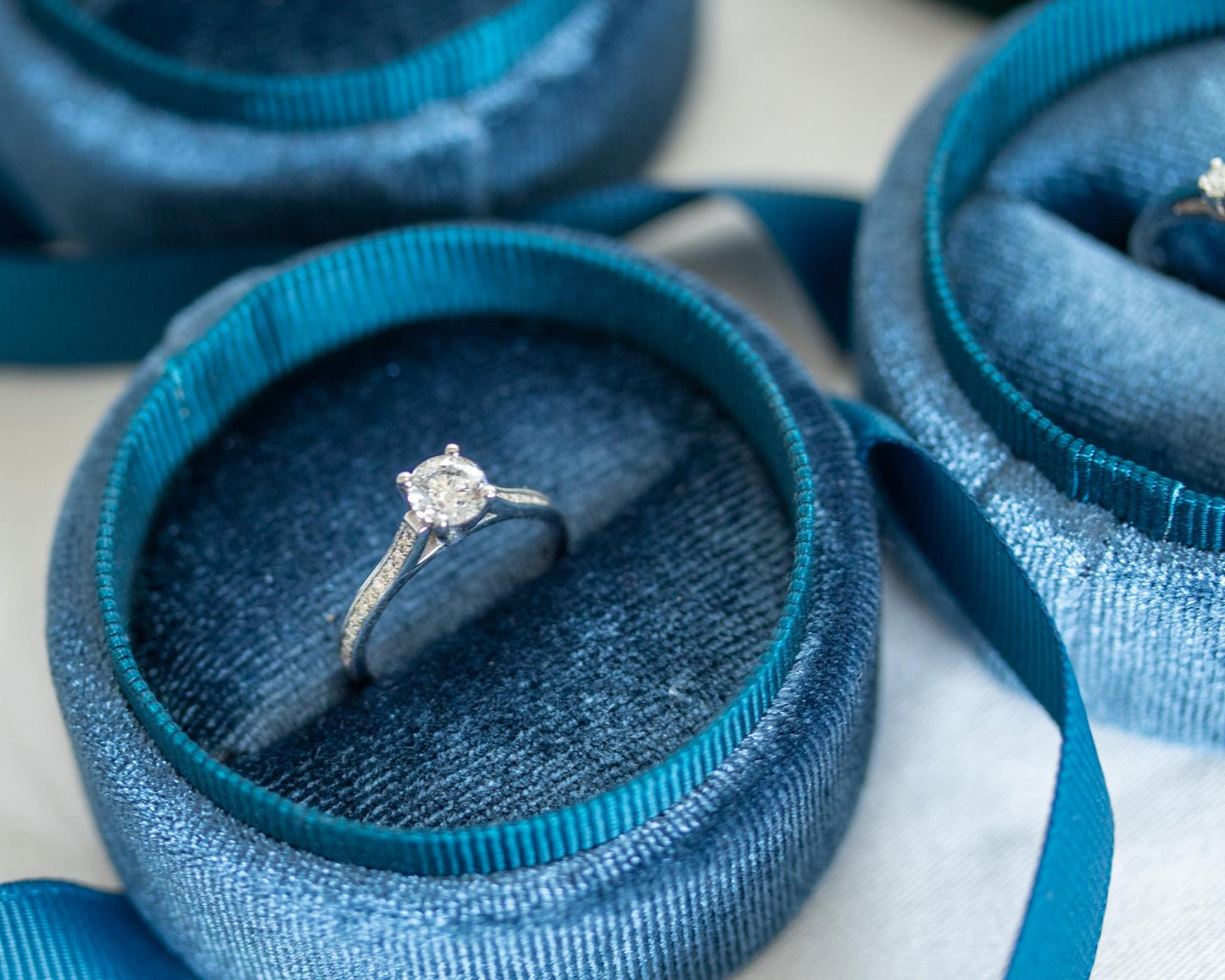 White gold engagement ring with round diamond and pavé band displayed in blue velvet jewelry box, elegant minimalist design