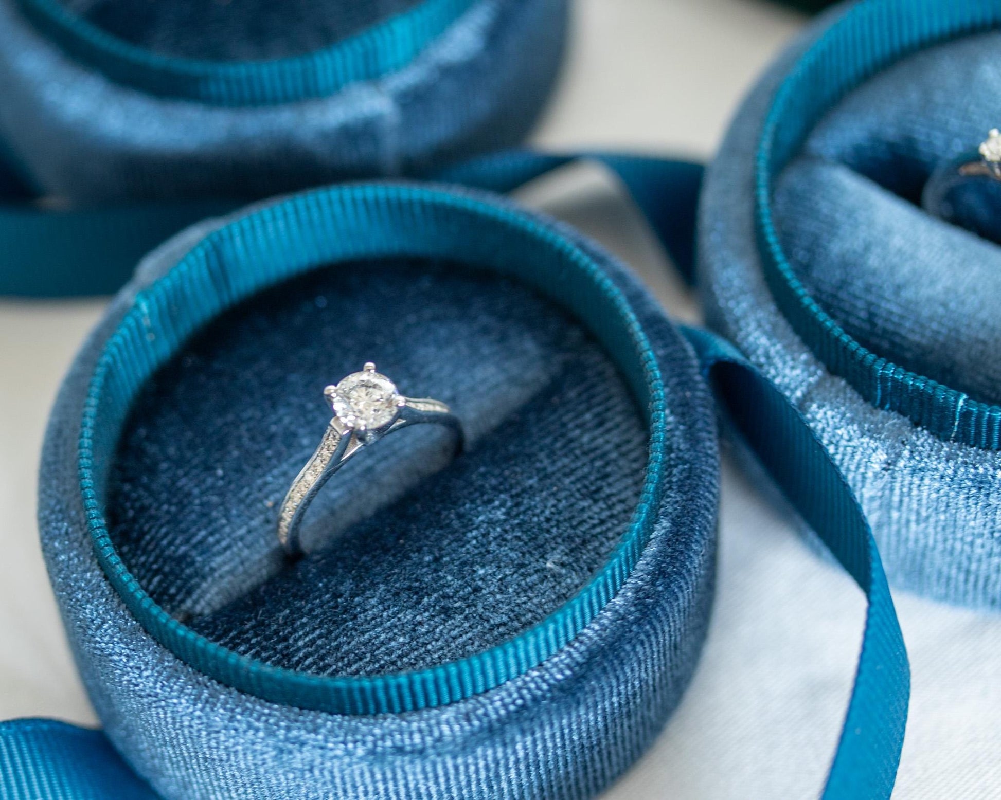 White gold engagement ring with round diamond and pavé band displayed in blue velvet jewelry box, elegant minimalist design