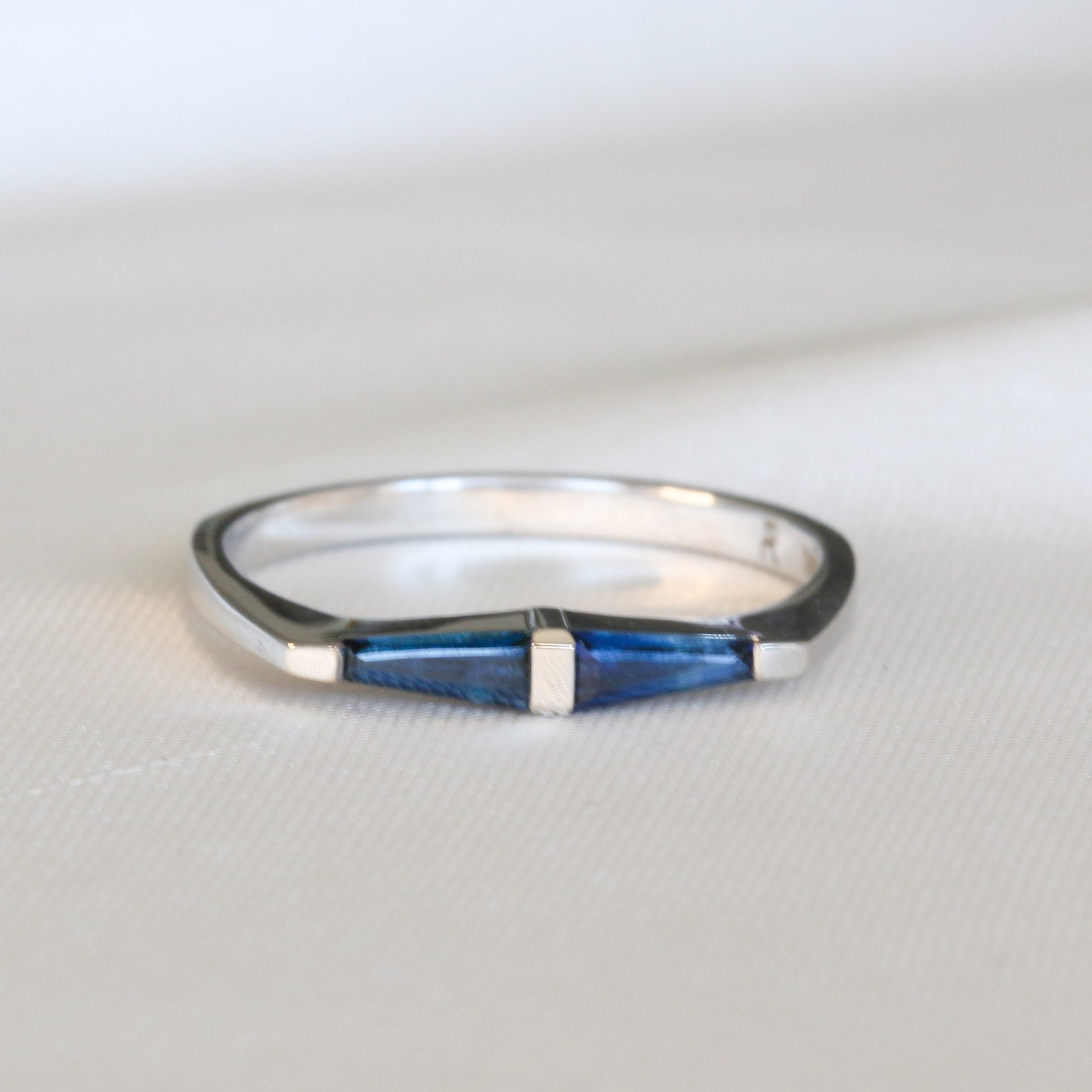 A 14K white gold ring with two natural blue tapered baguette cut sapphires on white background